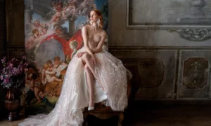 A model in a unique blush wedding dress by Papilio Boutique in Toronto, featuring delicate floral appliques and a flowing tulle skirt, poses in a classical, art-adorned room, epitomizing the luxury of designer wedding dresses.