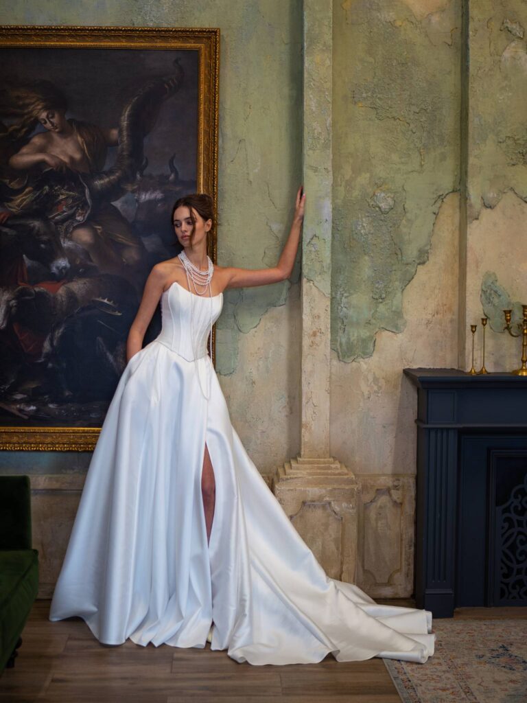 A bride posing in a sophisticated satin wedding dress with a high slit, reflecting the minimalist style prominent in 2025 wedding dress trends.