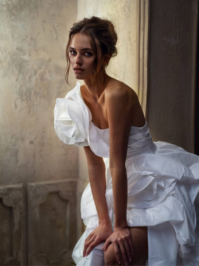 A bride wearing a unique wedding dress with a dramatic one-shoulder floral detail, showcasing bold elements of the 2025 wedding dress trends.