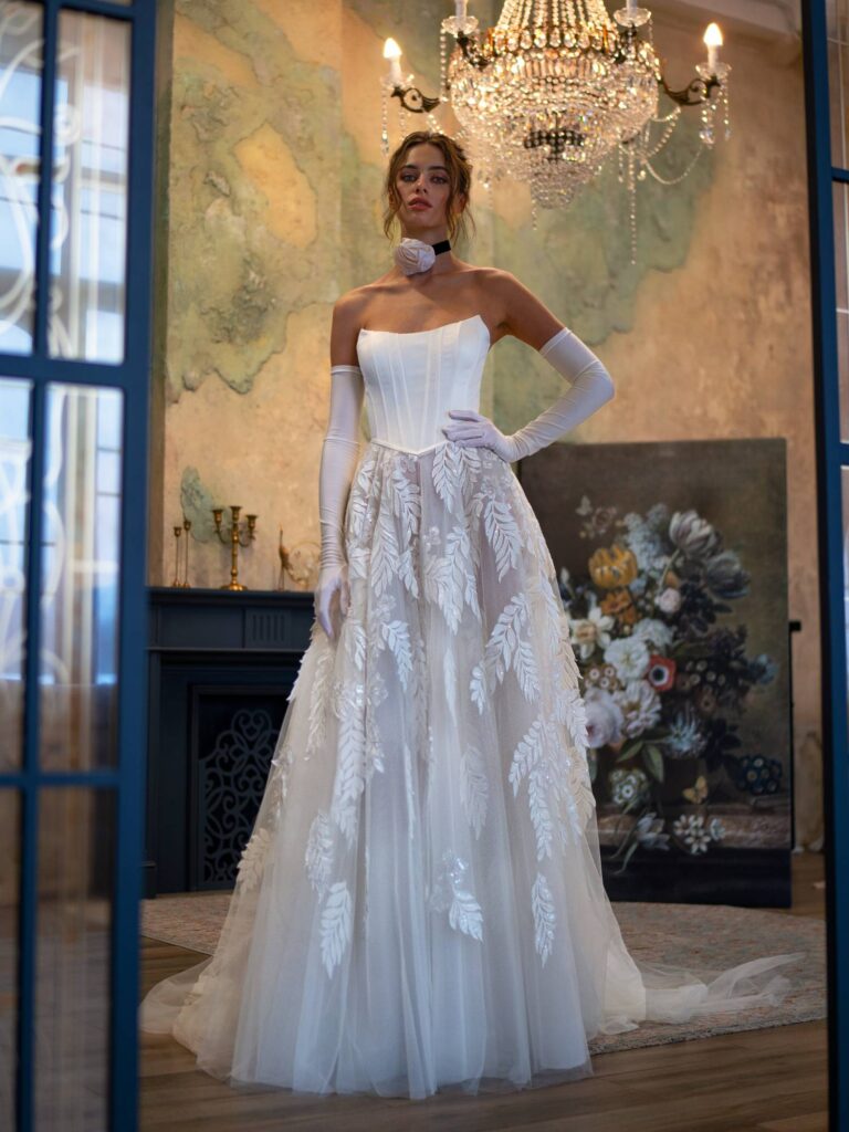 A bride standing elegantly in a wedding dress with delicate lace and transparent elements, epitomizing the ethereal lightness of the 2025 wedding dress trends.