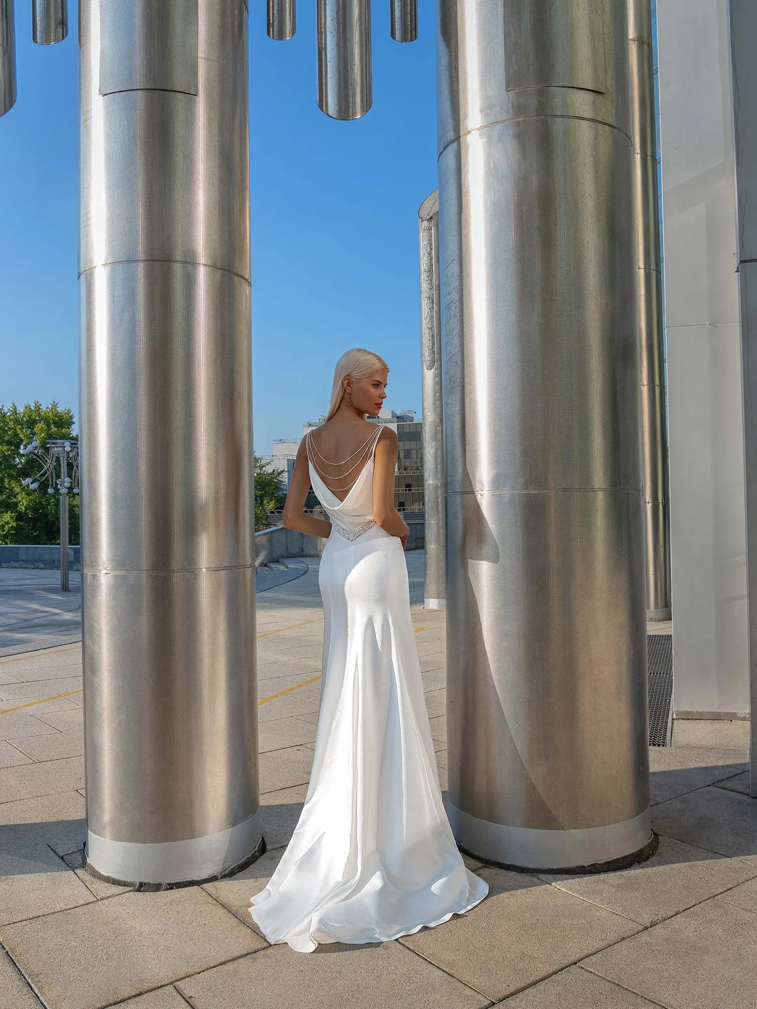 Elegant backless sheath wedding dress with delicate draped pearl accents, a deep V-back, and a long flowing train, ideal for tall brides. Find the Best Wedding Dress for Body Type at Papilio Boutique in Toronto.