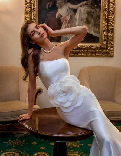 Model posing in a simple fitted wedding gown with a large accent flower, showcasing elegance at Papilio Boutique Toronto bridal store.