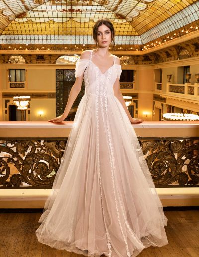 Elegant bride in an A-line gown with dramatic capes, set against a grand ballroom, by Papilio Boutique Toronto bridal store.