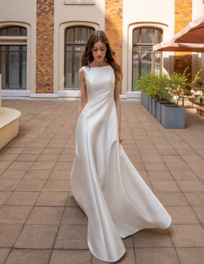 Simple and elegant bride in a boatneck gown with a statement bow, walking gracefully, by Papilio Boutique Toronto bridal store.