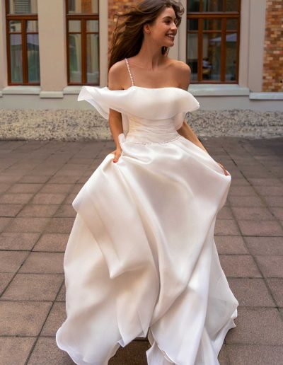 Bride in organza wedding gown with off-the-shoulder detail, by Papilio Boutique Toronto bridal store, joyfully dancing outdoors.