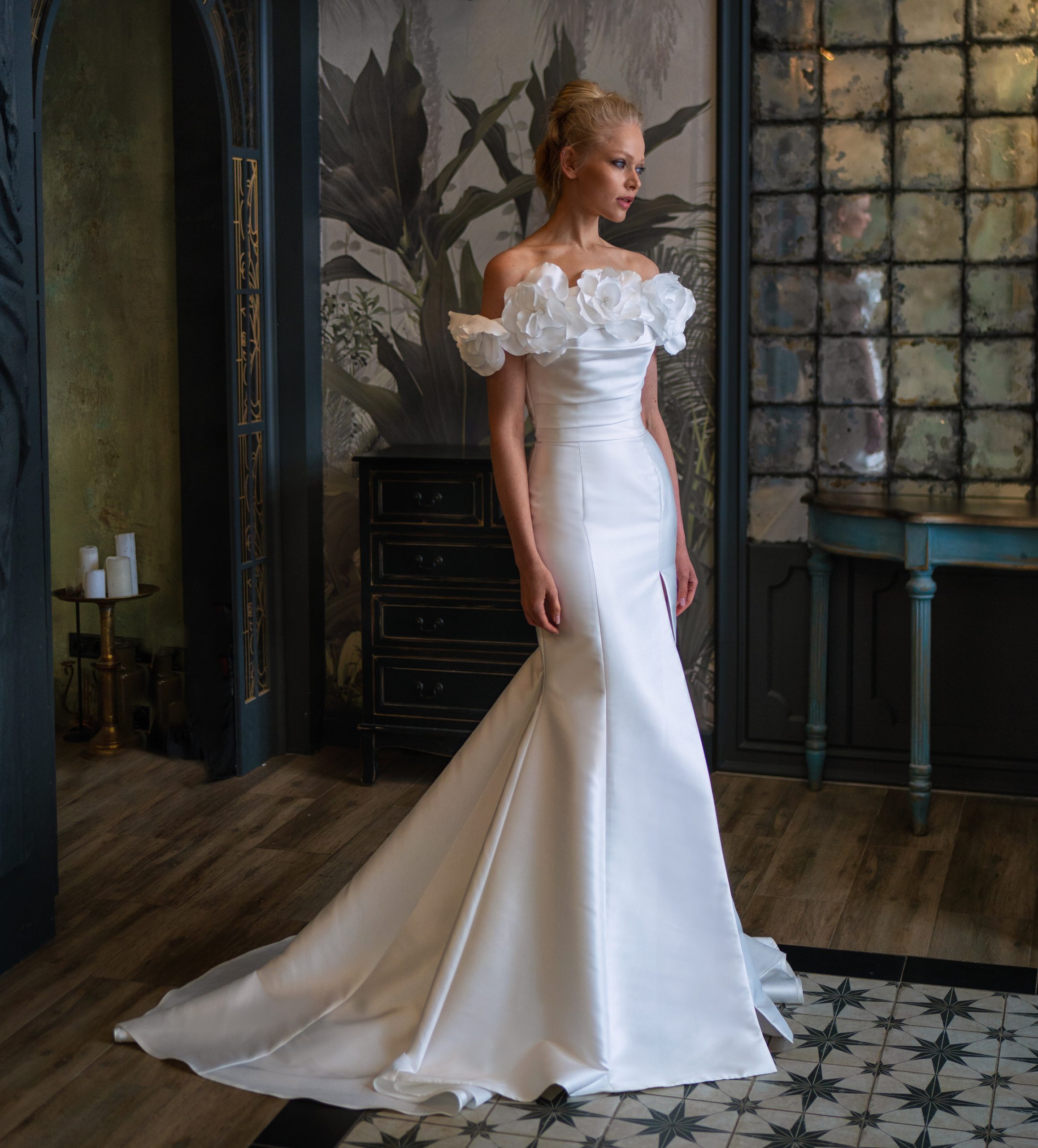 Elegant satin wedding dresses with a sleek, fitted silhouette and dramatic train, adorned with large white floral accents on the shoulders, perfect for brides in Toronto seeking a luxurious look.